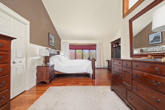 bedroom with high vaulted ceiling, wood finished floors, and a wainscoted wall