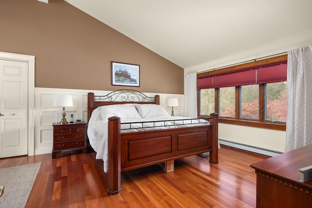 bedroom with wood finished floors, lofted ceiling, a baseboard heating unit, and a wainscoted wall