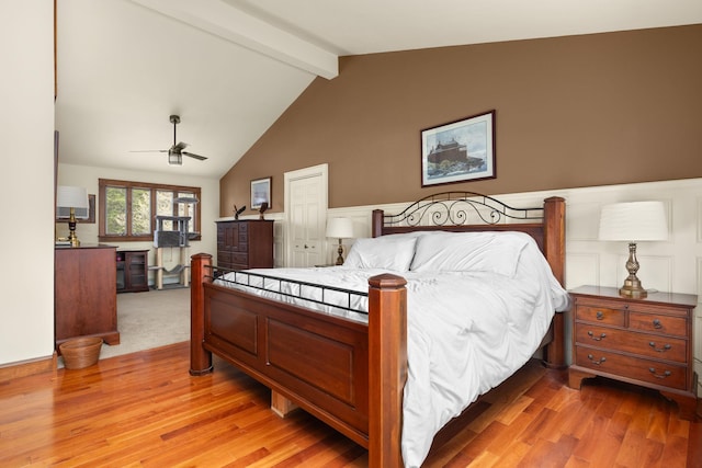 bedroom with light wood-style floors, vaulted ceiling with beams, and wainscoting