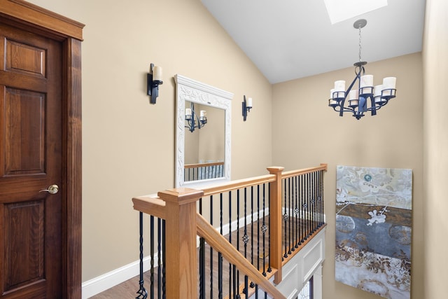 hall with a notable chandelier, vaulted ceiling with skylight, baseboards, an upstairs landing, and wood finished floors