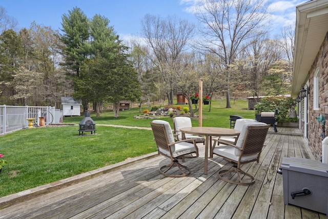 wooden deck featuring fence, outdoor dining space, a shed, a lawn, and an outdoor structure