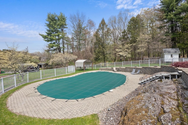 view of pool featuring fence, a storage unit, and an outbuilding