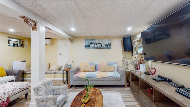 living area with a paneled ceiling, recessed lighting, wood finished floors, a wall mounted air conditioner, and baseboards