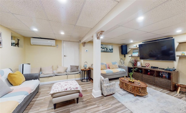 living area with a paneled ceiling, baseboards, an AC wall unit, and wood finished floors