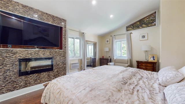 bedroom with a wall unit AC, a fireplace, wood finished floors, baseboards, and vaulted ceiling