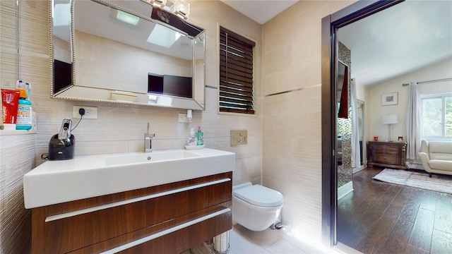 bathroom with toilet, vanity, tile walls, vaulted ceiling, and wood-type flooring