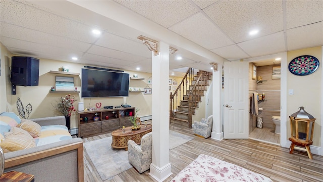 living area featuring stairs, a drop ceiling, wood finished floors, and a baseboard radiator