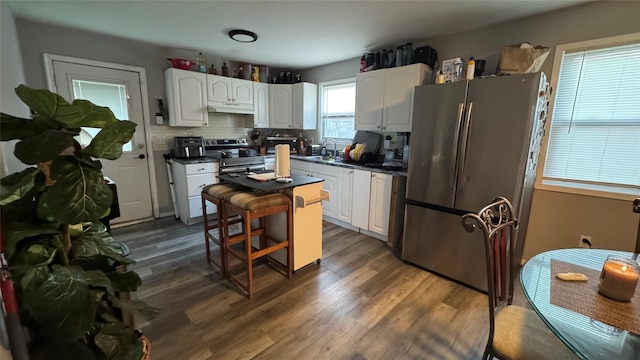 kitchen featuring dark countertops, appliances with stainless steel finishes, under cabinet range hood, white cabinetry, and a sink