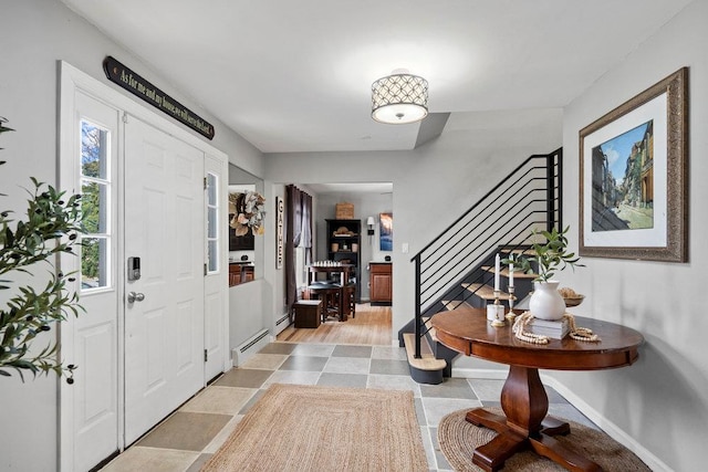 foyer entrance with a baseboard radiator, stairway, and baseboards