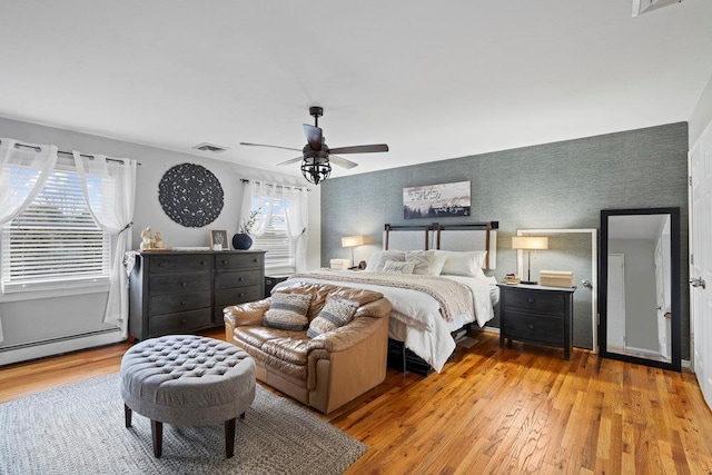 bedroom with ceiling fan, visible vents, light wood-style floors, baseboard heating, and wallpapered walls