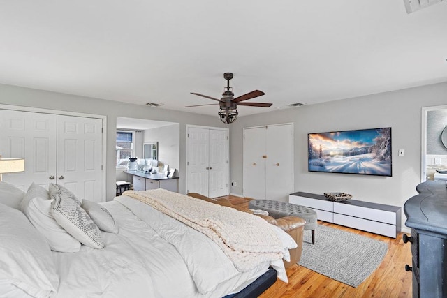 bedroom with ceiling fan, visible vents, two closets, and wood finished floors