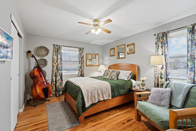 bedroom with light wood-style floors, multiple windows, baseboard heating, and a ceiling fan