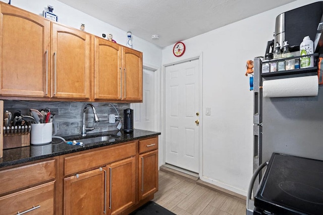 kitchen with black electric range, light wood-style flooring, decorative backsplash, a sink, and dark stone counters