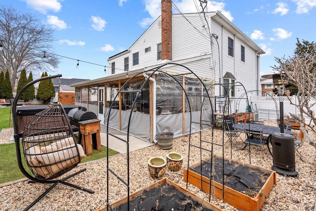 back of property featuring a patio, a chimney, a sunroom, fence, and a garden