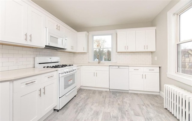 kitchen featuring radiator, white appliances, white cabinetry, and a wealth of natural light