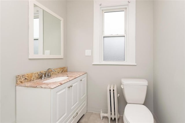 half bathroom with radiator heating unit, baseboards, vanity, and toilet