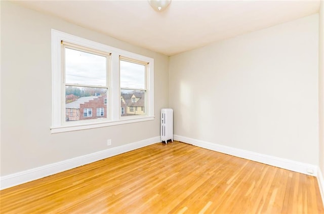 empty room with baseboards, light wood-style floors, and radiator