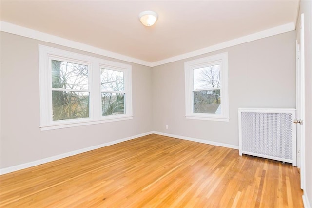 empty room with baseboards, ornamental molding, light wood-style flooring, and radiator