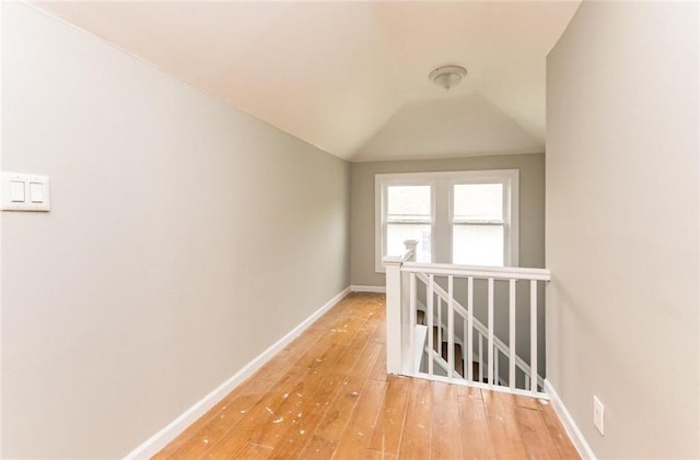 hall with wood-type flooring, baseboards, vaulted ceiling, and an upstairs landing