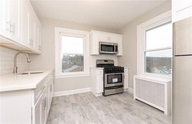 kitchen with light countertops, radiator heating unit, appliances with stainless steel finishes, white cabinets, and a sink