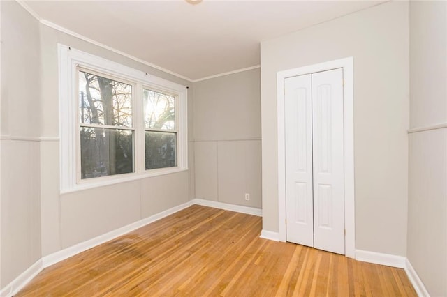 unfurnished bedroom featuring light wood-style flooring, a closet, baseboards, and crown molding