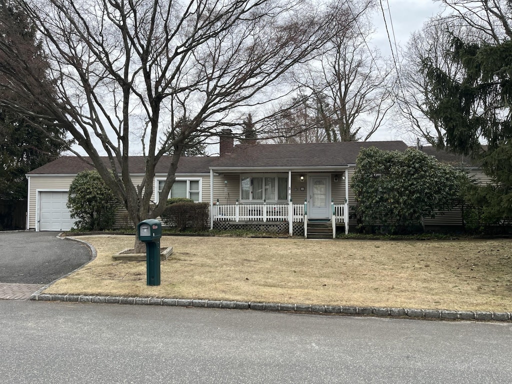 view of front of house featuring a garage, covered porch, a chimney, and a front lawn