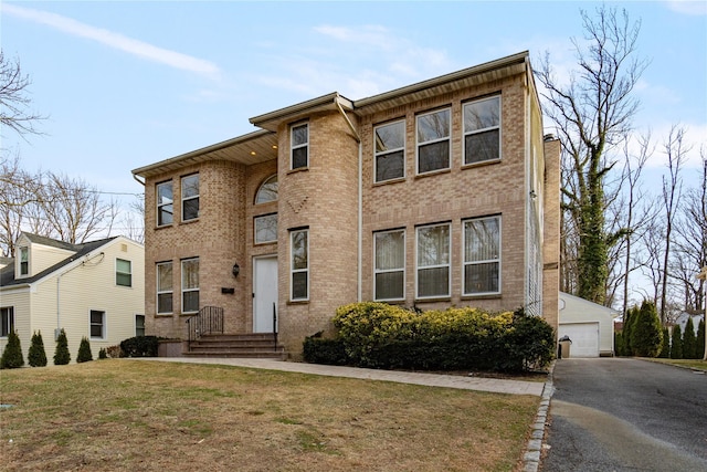 view of front facade featuring a garage, an outbuilding, brick siding, and a front yard