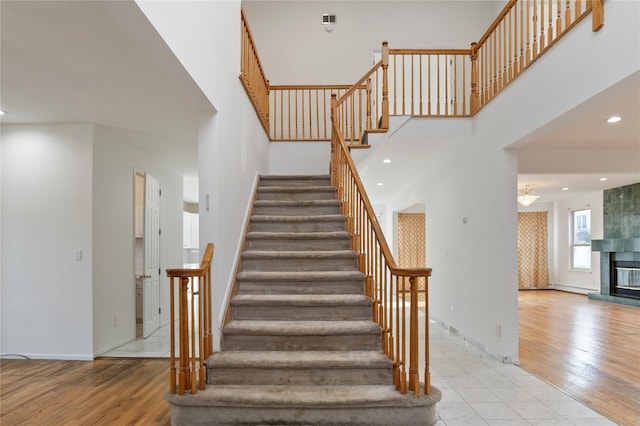 stairway with a tiled fireplace, wood finished floors, a towering ceiling, and baseboards