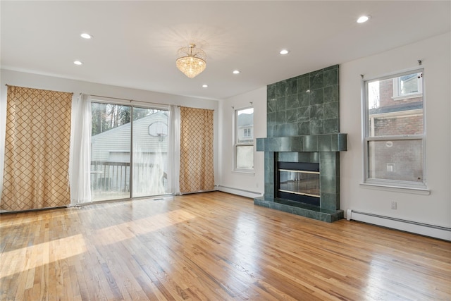 unfurnished living room featuring plenty of natural light, wood finished floors, a baseboard radiator, and a tile fireplace