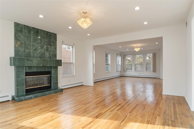 unfurnished living room featuring wood-type flooring, a notable chandelier, a baseboard heating unit, baseboard heating, and a tiled fireplace