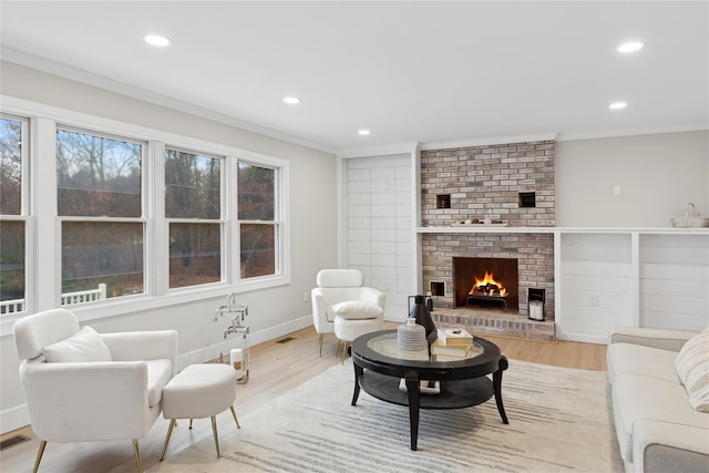 living room with light wood-style floors, a fireplace, ornamental molding, and recessed lighting