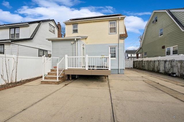 rear view of house with a fenced backyard, roof mounted solar panels, a patio, and a wooden deck