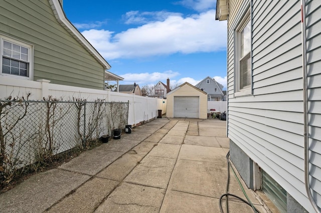 view of patio / terrace featuring a garage, fence, concrete driveway, and an outdoor structure