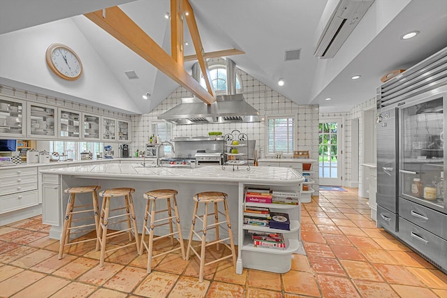 2 Aspen Pl, Great Neck, NY 11021 - kitchen with light countertops, open shelves, a large island with sink, glass insert cabinets, and a kitchen breakfast bar
