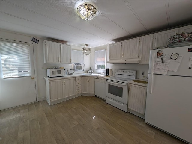 kitchen with under cabinet range hood, white appliances, a sink, light countertops, and light wood finished floors