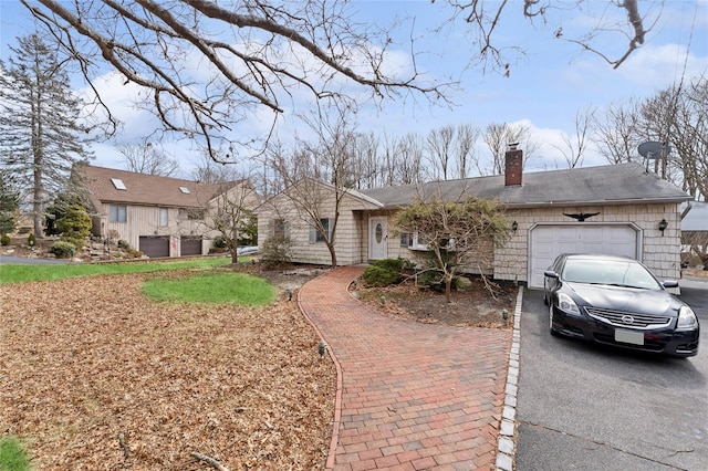 ranch-style home featuring aphalt driveway, an attached garage, and a chimney