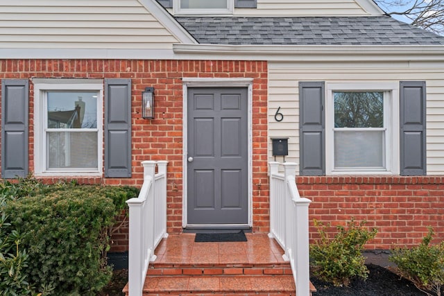 property entrance featuring a shingled roof and brick siding