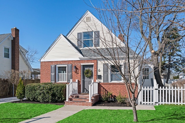 view of front facade with brick siding, a front lawn, and fence