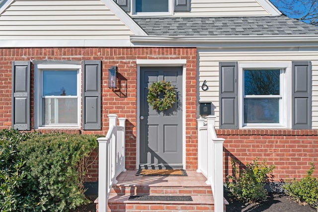 doorway to property featuring brick siding and roof with shingles