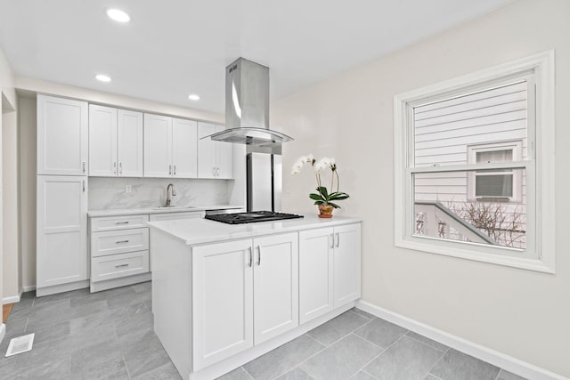 kitchen featuring black gas stovetop, a sink, a peninsula, island range hood, and light countertops