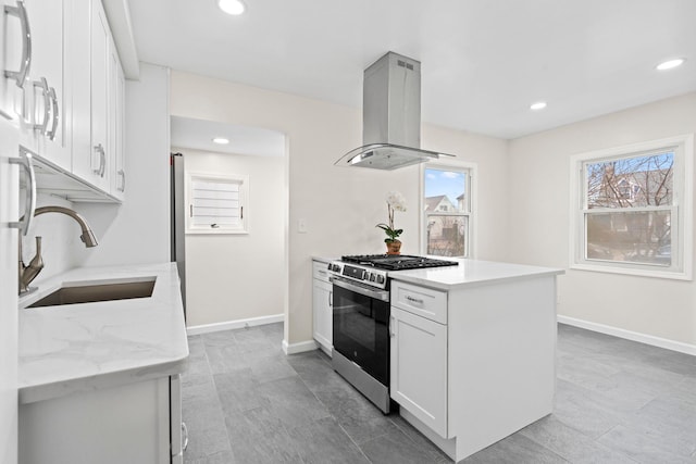 kitchen with island exhaust hood, stainless steel range with gas cooktop, baseboards, and a sink