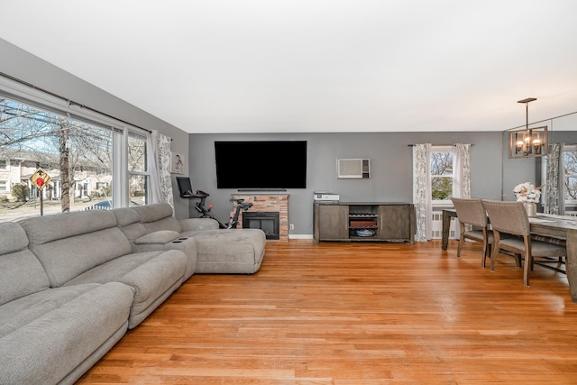 living room with a wall mounted air conditioner, light wood-style floors, an inviting chandelier, and a stone fireplace