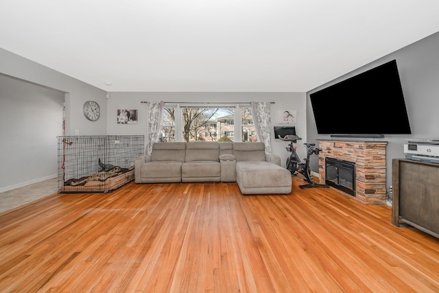 unfurnished living room featuring a stone fireplace, baseboards, and wood finished floors