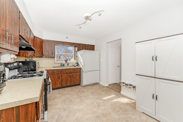 kitchen featuring baseboards, freestanding refrigerator, light countertops, under cabinet range hood, and gas range