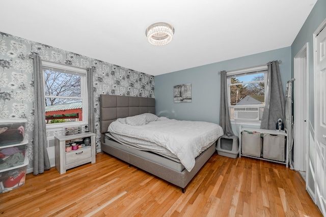 bedroom with light wood-style flooring, cooling unit, wallpapered walls, and an accent wall