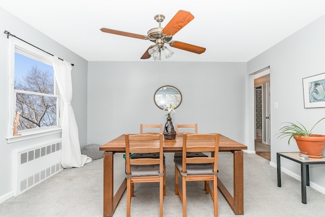 dining space featuring radiator, a ceiling fan, baseboards, and light carpet