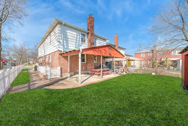 back of house with a lawn, a patio, a fenced backyard, brick siding, and a chimney