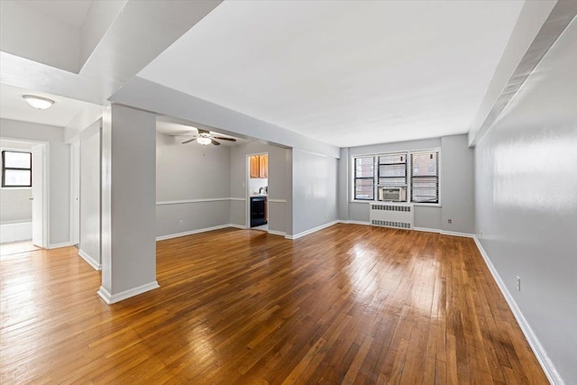 unfurnished room featuring ceiling fan, radiator heating unit, wood-type flooring, and plenty of natural light