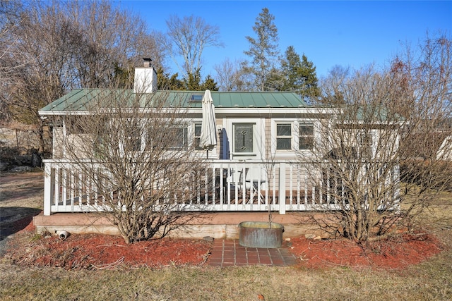 view of front facade featuring metal roof, covered porch, a chimney, and a standing seam roof