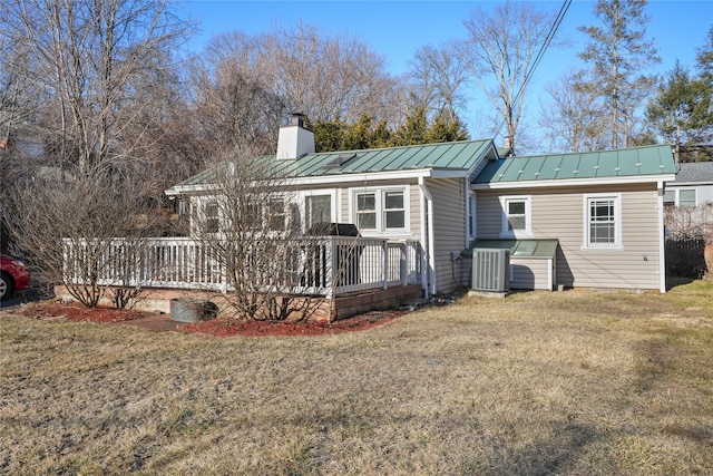 back of property featuring central air condition unit, a chimney, metal roof, a yard, and a standing seam roof